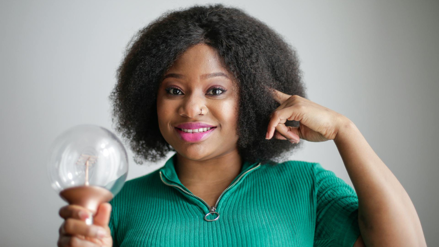 Frau hält Glühbirne über dem Kopf – Symbol für Inspiration, kreative Ideen und das Finden der eigenen Begabung