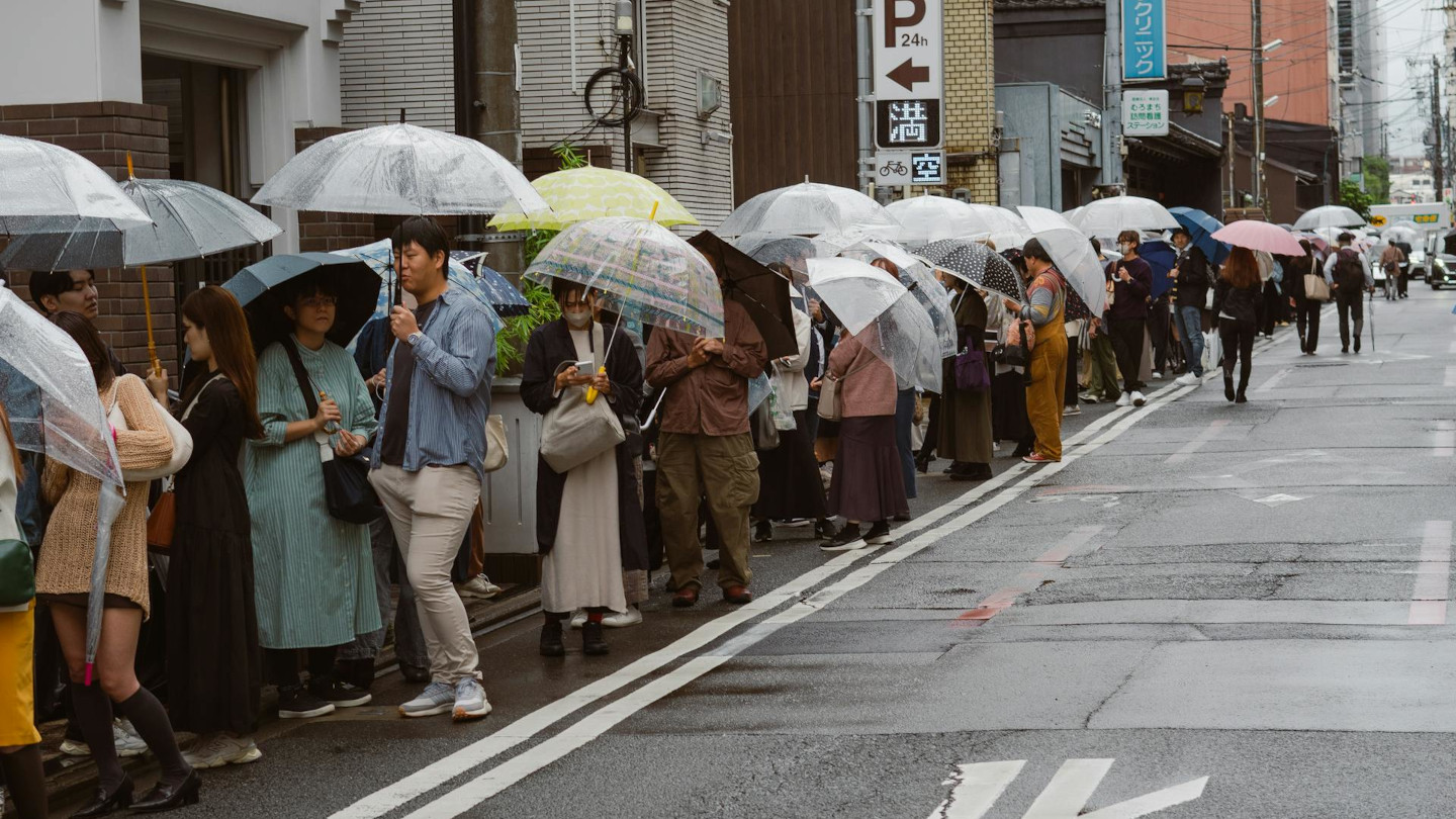 Menschen mit Regenschirmen stehen geordnet auf einer verregneten Straße in Japan – Beispiel für Rücksicht und Rücksichtnahme im Alltag.